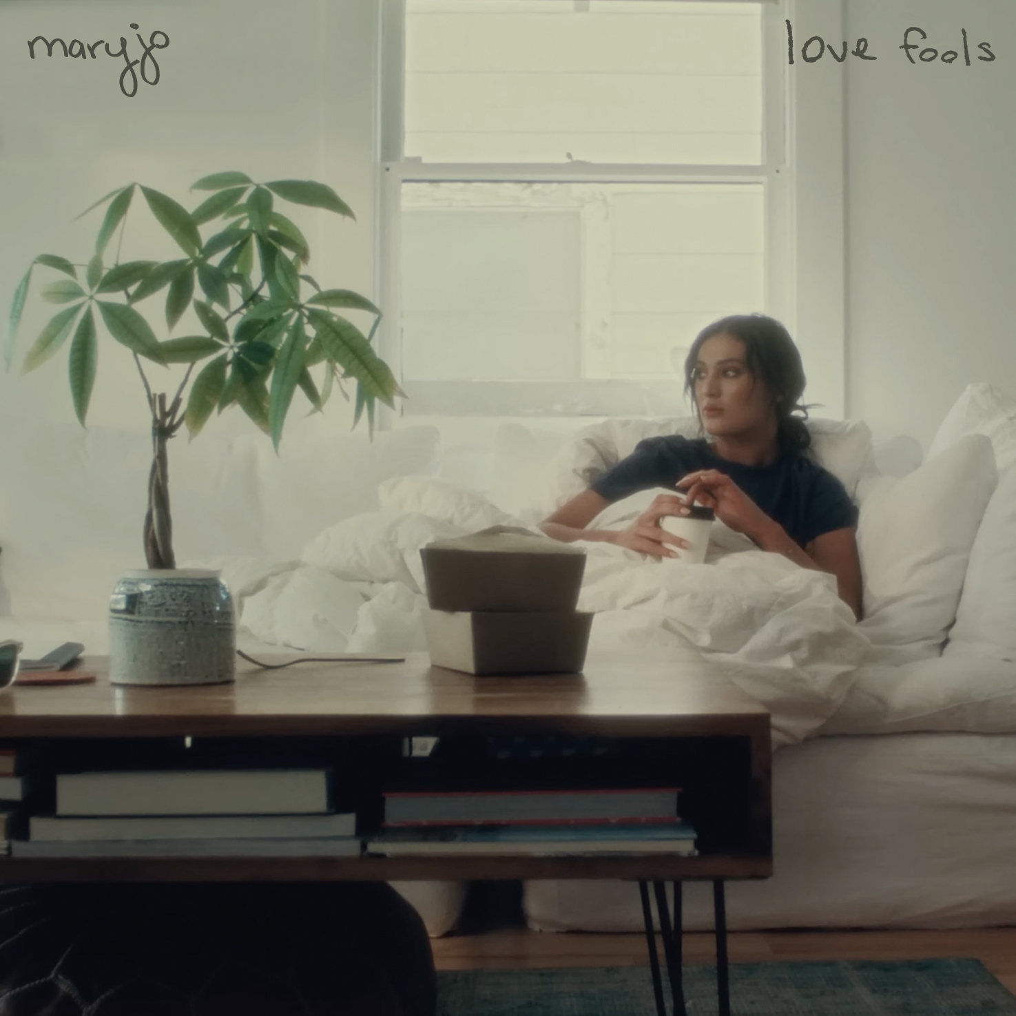 The cover art for Love Fools: maryjo stands at a front door holding a cake that says ‘Love Fools’.